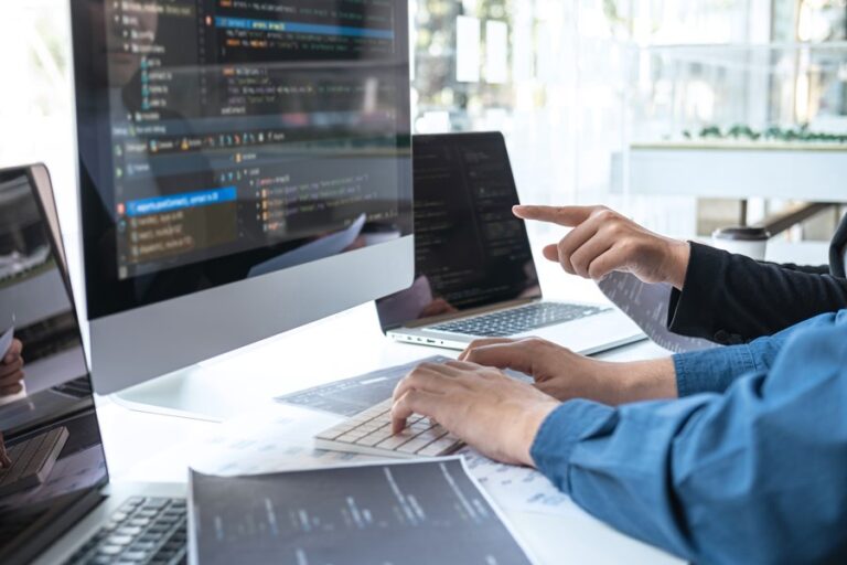 Two people at a desk looking at a computer screen with code on it
